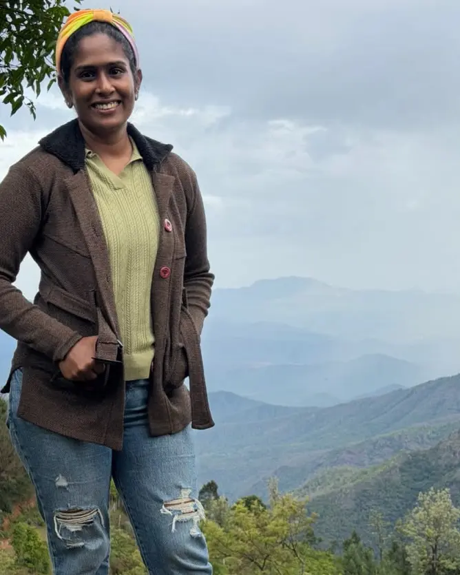Dr. Indhu Nagaiah smiling on a hilltop overlooking misty mountain ranges